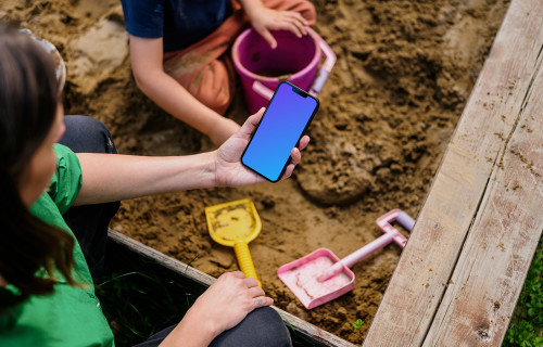 Woman holding an iPhone 13 mockup in sandpit