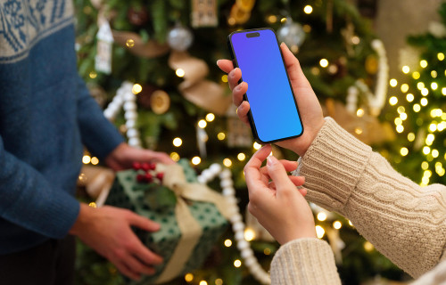 Woman holding an iPhone mockup next to the Christmas tree