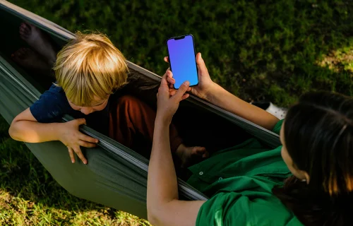 Woman laying in a hammock and typing on an iPhone 13 mockup