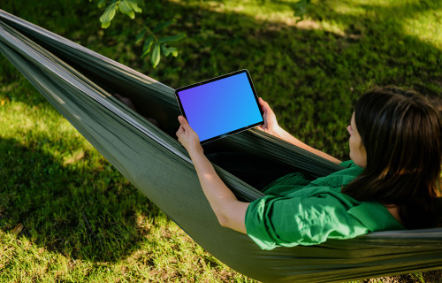 Woman laying in hammock while holding a tablet