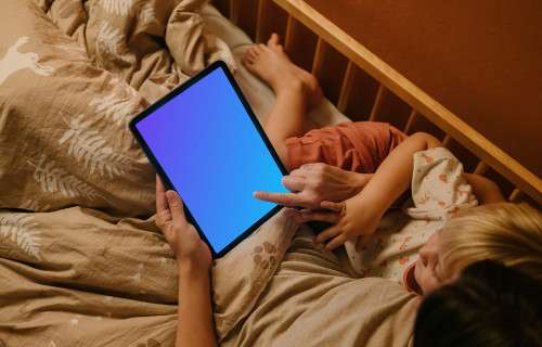 Woman with a child typing on an iPad mockup in bed