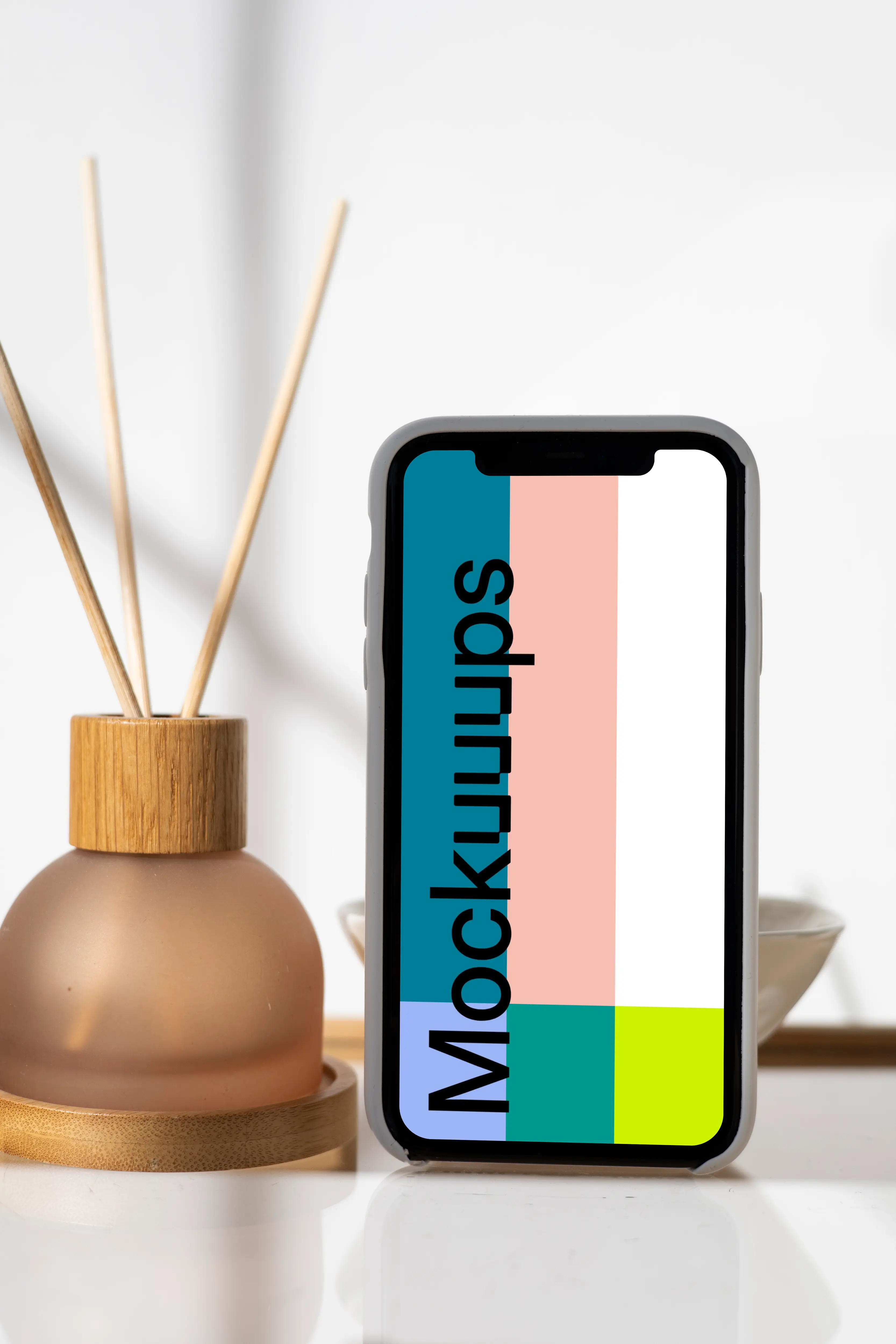 iPhone mockup standing vertically on a table next to a vase with empty sticks in them.