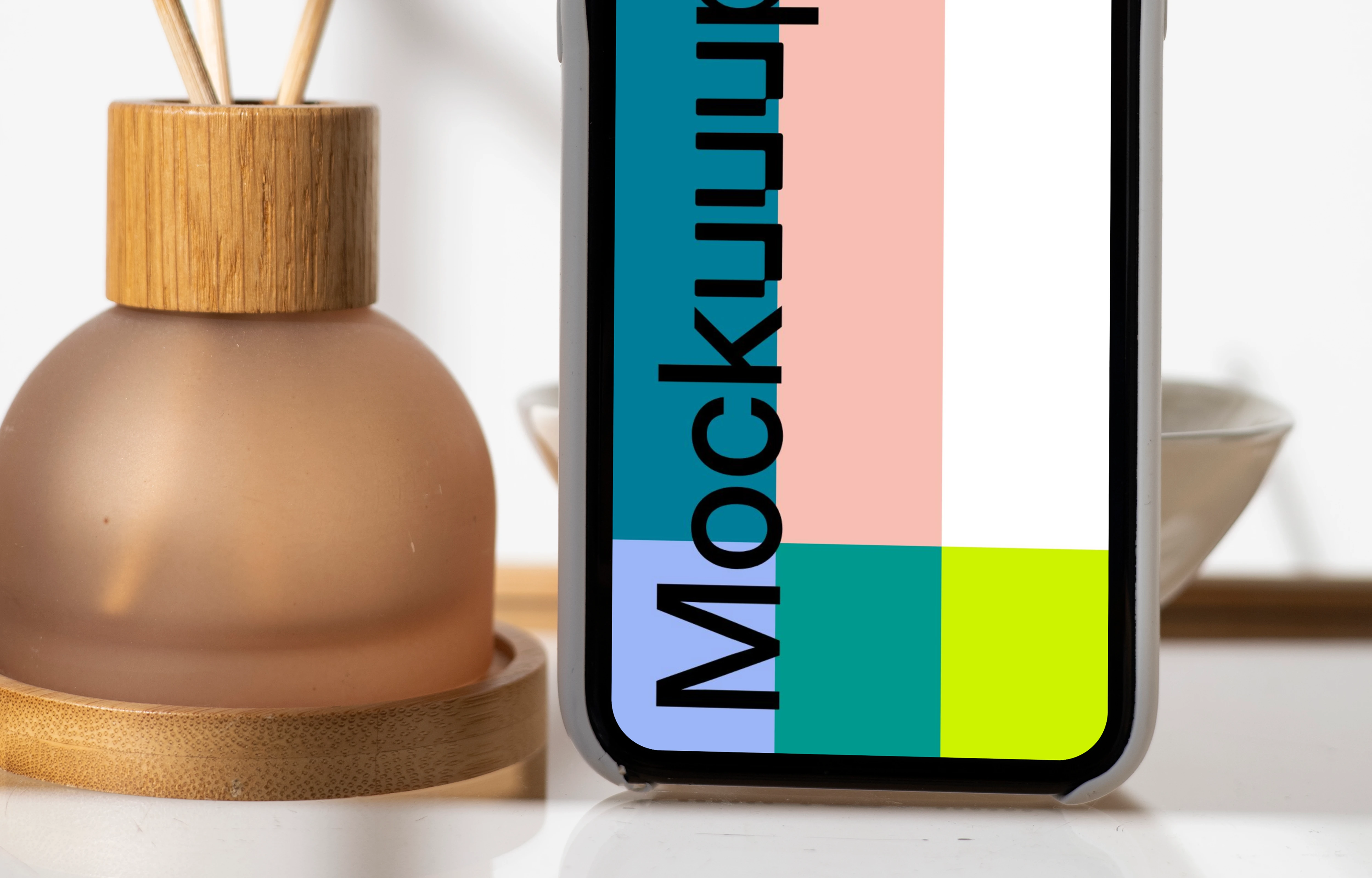 iPhone mockup standing vertically on a table next to a vase with empty sticks in them.