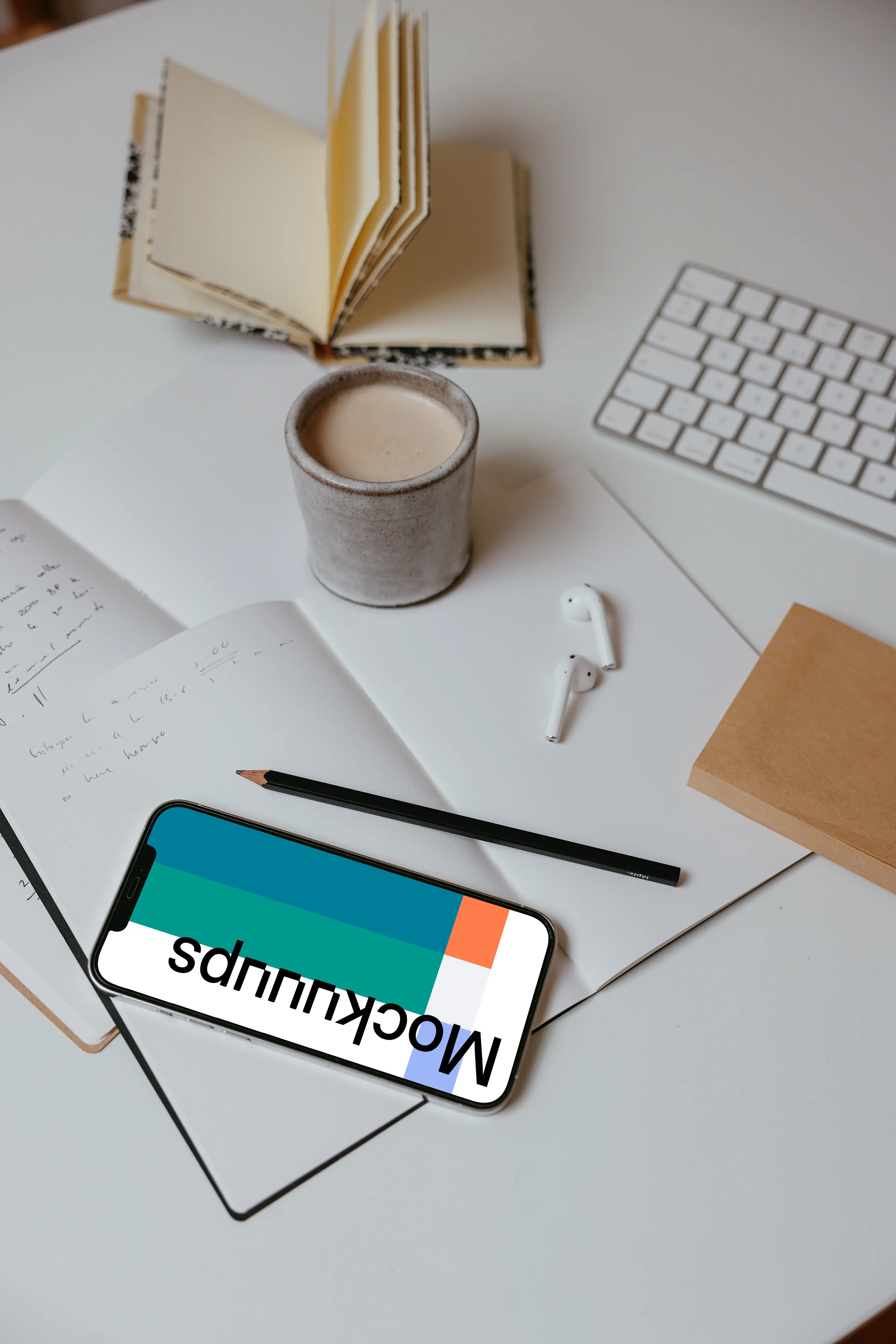 iPhone mockup on a table with books and a wireless keyboard by the side.