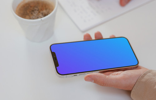 User holding iPhone and writing on a notebook beside a cup of coffee