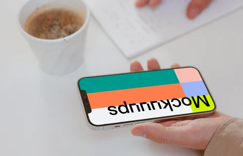 User holding iPhone and writing on a notebook beside a cup of coffee