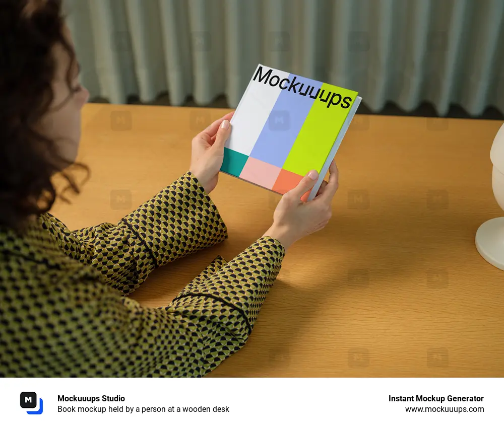 Book mockup held by a person at a wooden desk