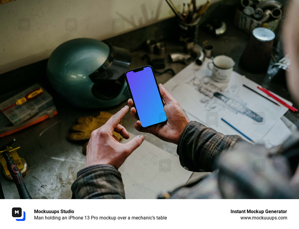 Man holding an iPhone 13 Pro mockup over a mechanic’s table