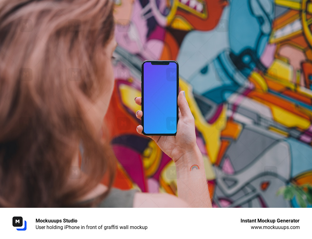 User holding iPhone in front of graffiti wall mockup
