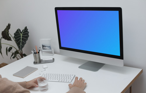 iMac on a white table with a cup of water