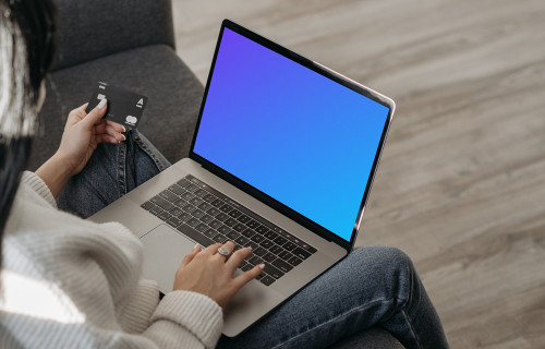 Mockup of female user on a couch shopping online with her grey MacBook and a MasterCard in hand