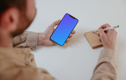 User holding an iPhone and writing into a sticky note mockup