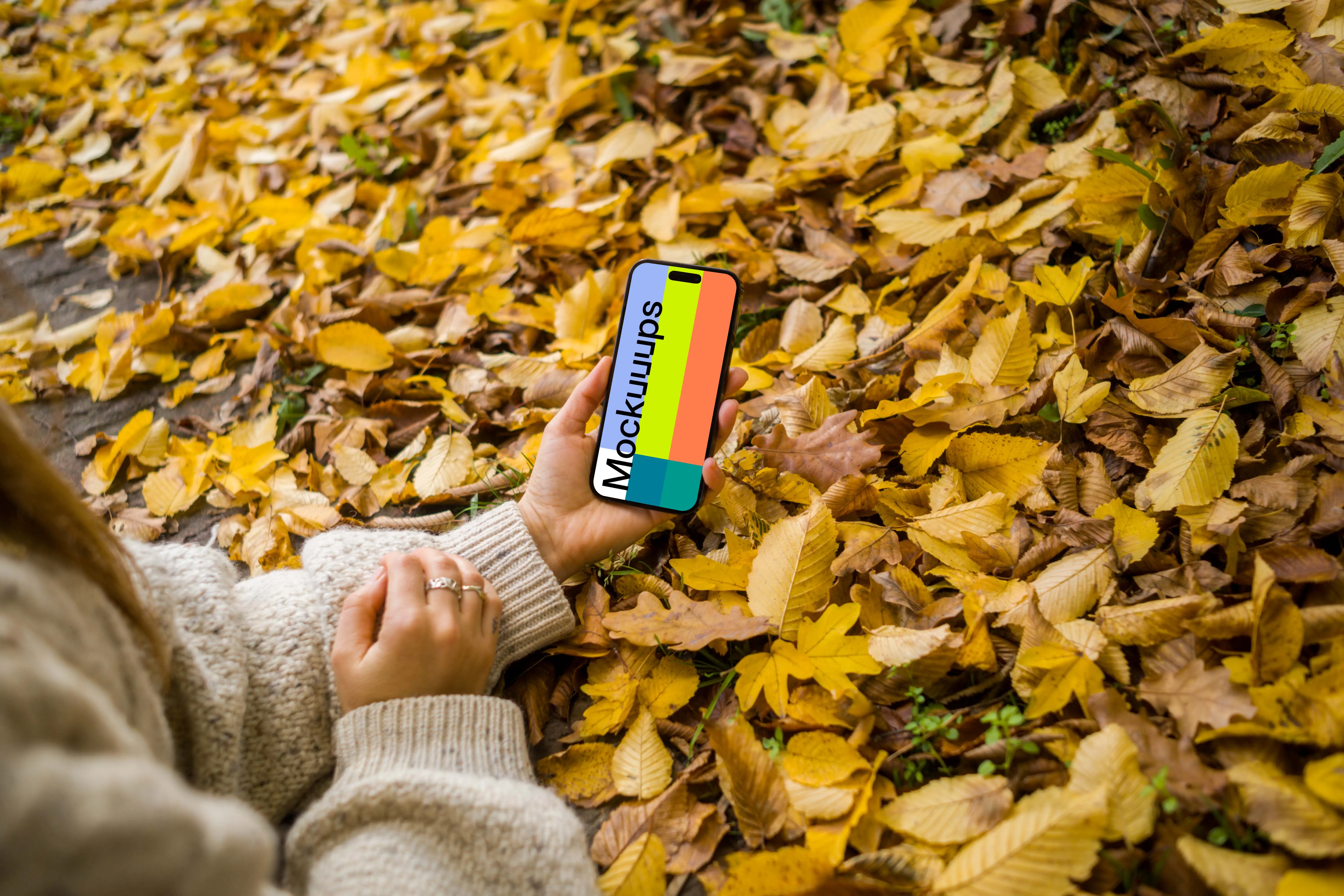 Hand holding an iPhone in the autumn leaves mockup