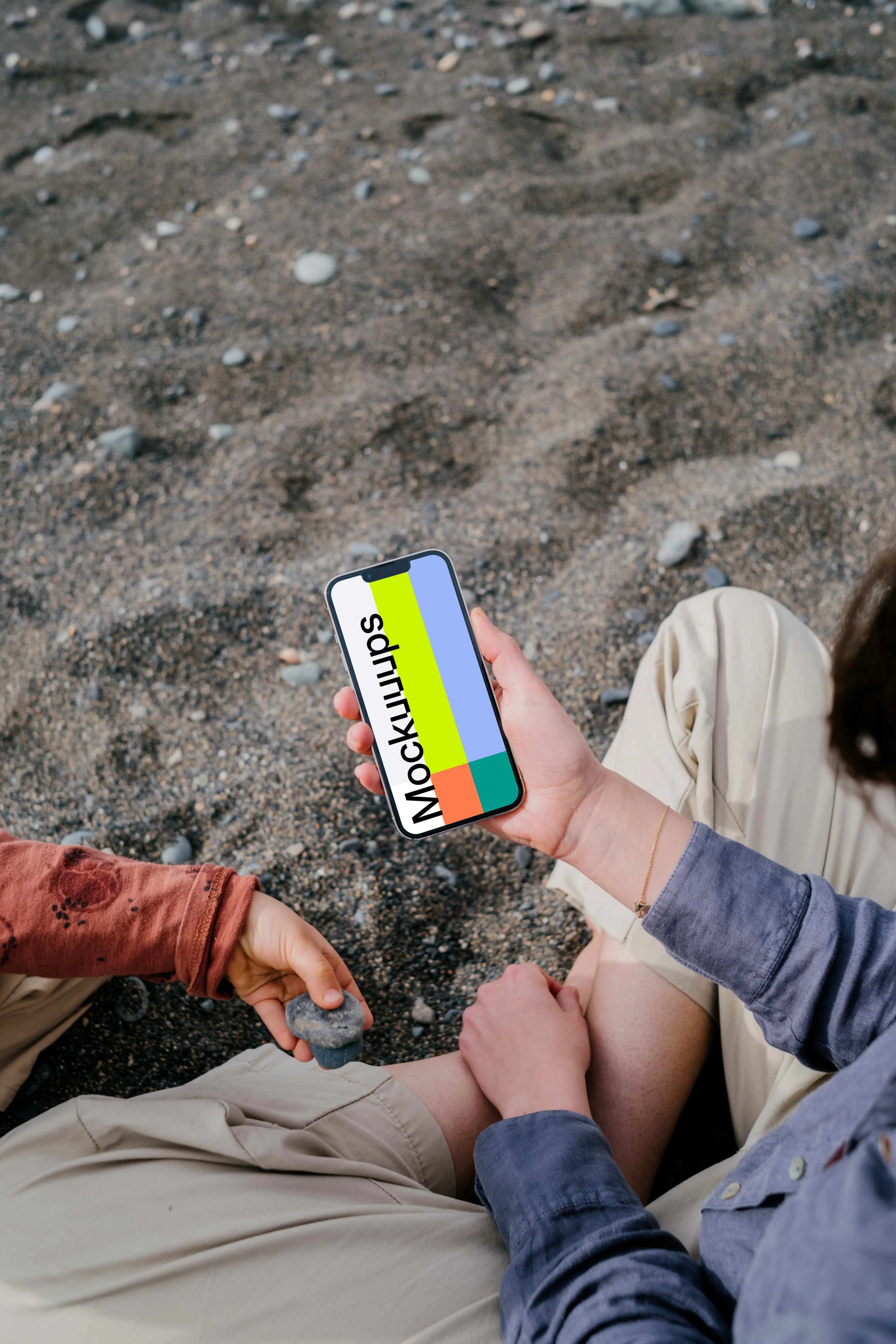 iPhone 13 Pro mockup held by a user sitting on sand