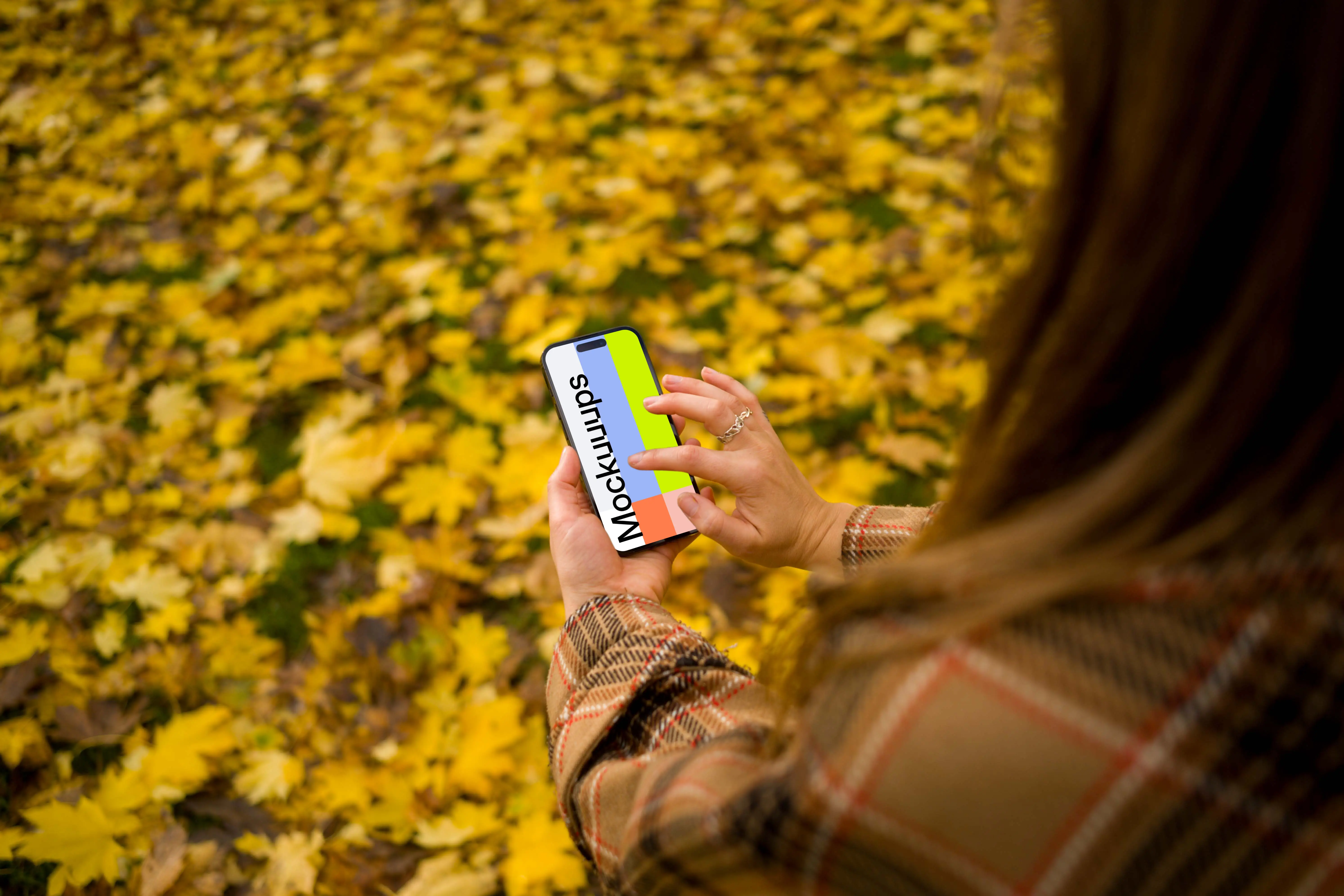 Woman typing on an iPhone 14 Pro in autumn theme mockup