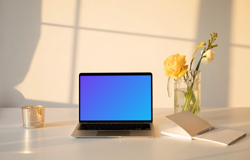 MacBook mockup on a table with a flower vase and an exercise book at the side.