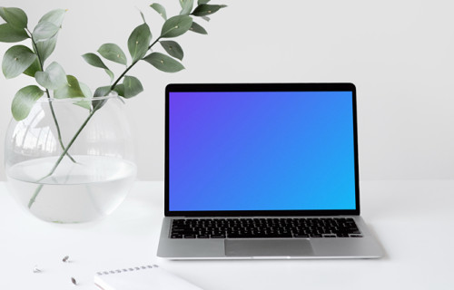 MacBook mockup on a white table with a bowl-shaped flower vase at the side