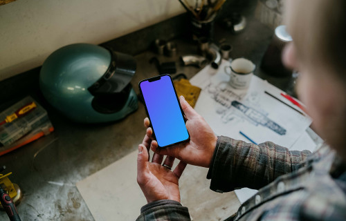 Man holding an iPhone 13 Pro mockup over a mechanic work table