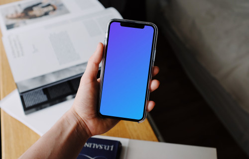 iPhone 12 Pro mockup retenido por un usuario por encima de los libros de texto
