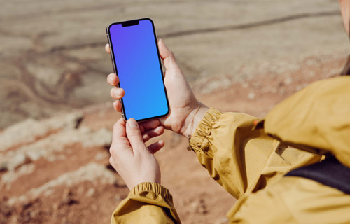 iPhone 13 Pro mockup sostenido por un usuario en una playa de arena