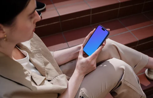 iPhone 16 mockup held by a woman on outdoor steps