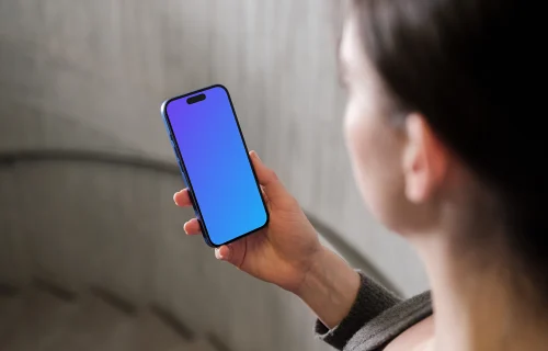 iPhone 16 mockup held in a woman's hand against concrete background