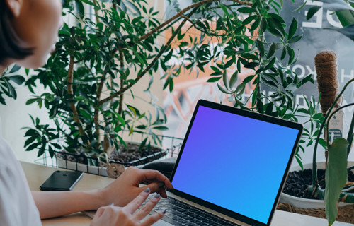 MacBook Air mockup in use by a lady with a lot of plants in the background