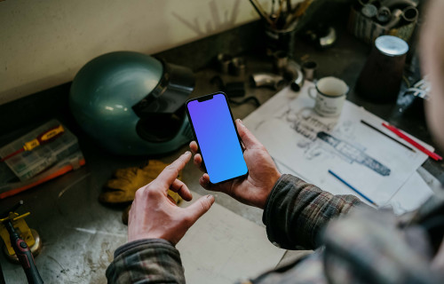 Man holding an iPhone 13 Pro mockup over a mechanic’s table