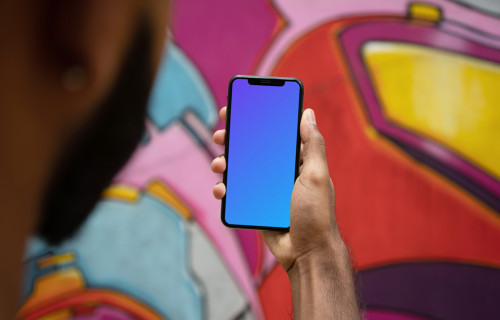 User holding iPhone in front of graffiti mockup