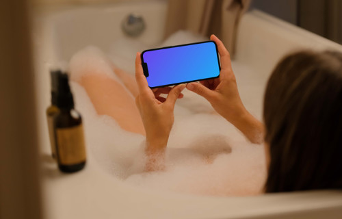 Woman in bath holding an iPhone 13 mockup