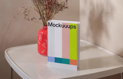 B-format book mockup on a white table with a red vase