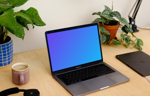 Grey MacBook Pro mockup with a coffee mug and an iPad at the side.