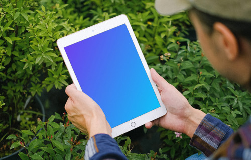 iPad Mini mockup held by male user in a garden.
