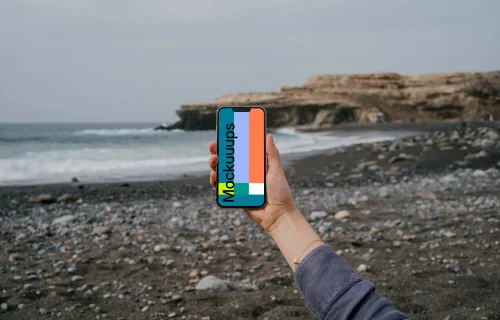 iPhone 13 Pro mockup held by a user against the ocean