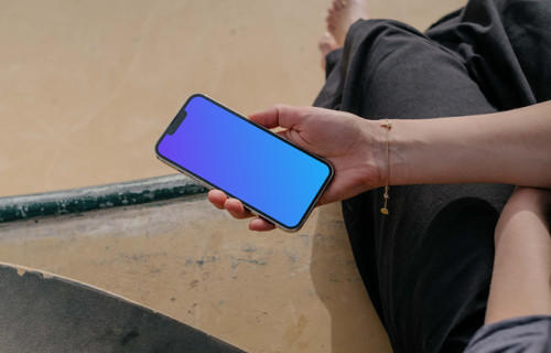 iPhone 13 Pro mockup held by a user seated next to a skateboard