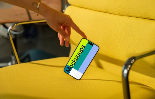 mockup iPhone 15 Pro avec interaction avec la main sur une chaise jaune