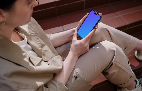 iPhone 16 mockup held by a woman on outdoor steps