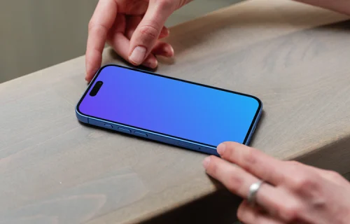 iPhone 16 mockup on a wooden surface with a hand interacting