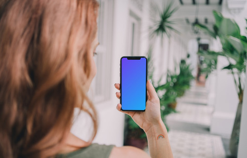iPhone mockup held by user in a plant-filled corridor