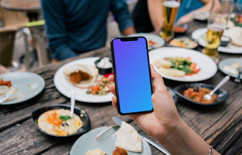 iPhone mockup in a user’s hand at dinner table