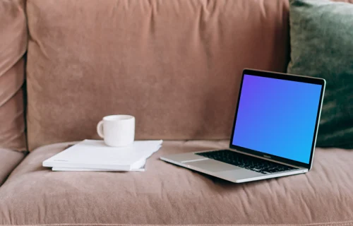 MacBook Pro mockup on a red sofa beside a couple of notepads