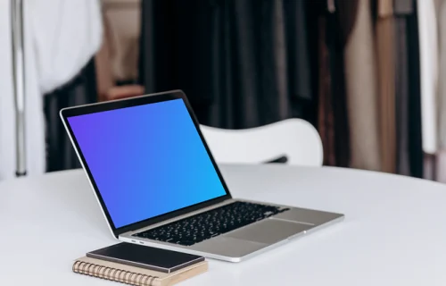 MacBook Pro mockup on a work table beside phone and notepad