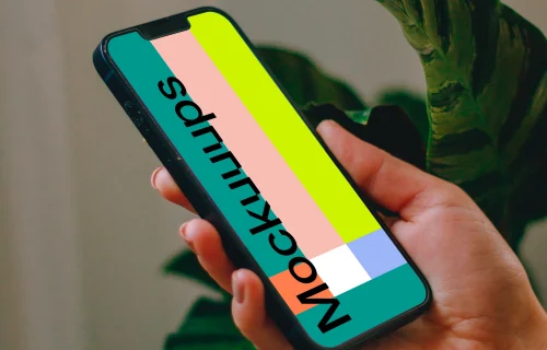 Person holding an iPhone 13 mockup with a plant in the background