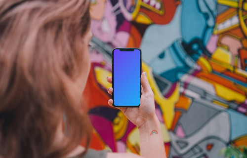 User holding iPhone in front of graffiti wall mockup