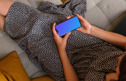Woman sitting on sofa holding an iPhone 13 mockup