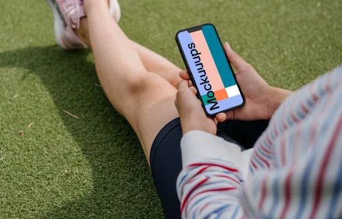 Young woman holding a smartphone mockup on a grass