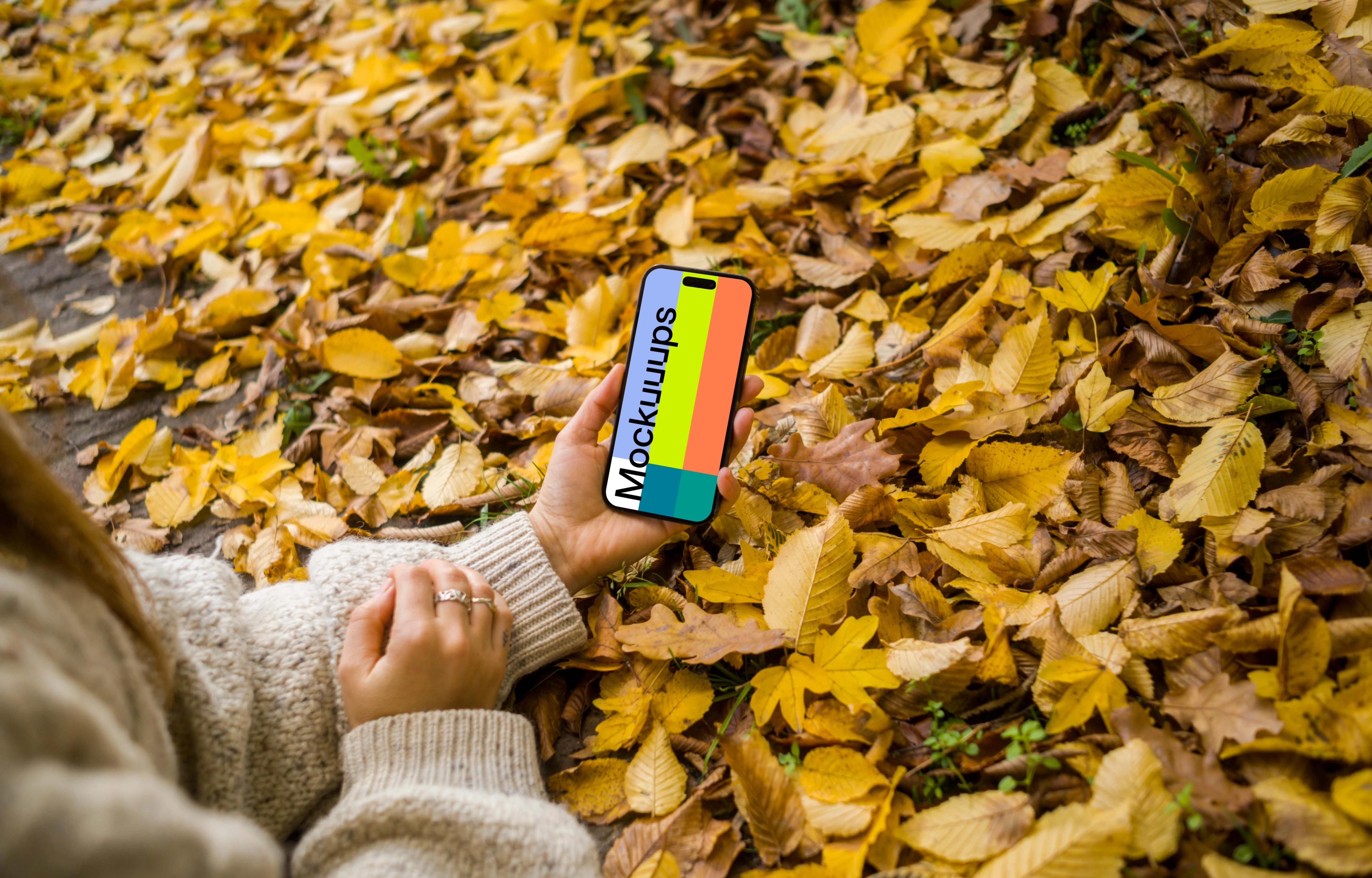 Hand holding an iPhone in the autumn leaves mockup