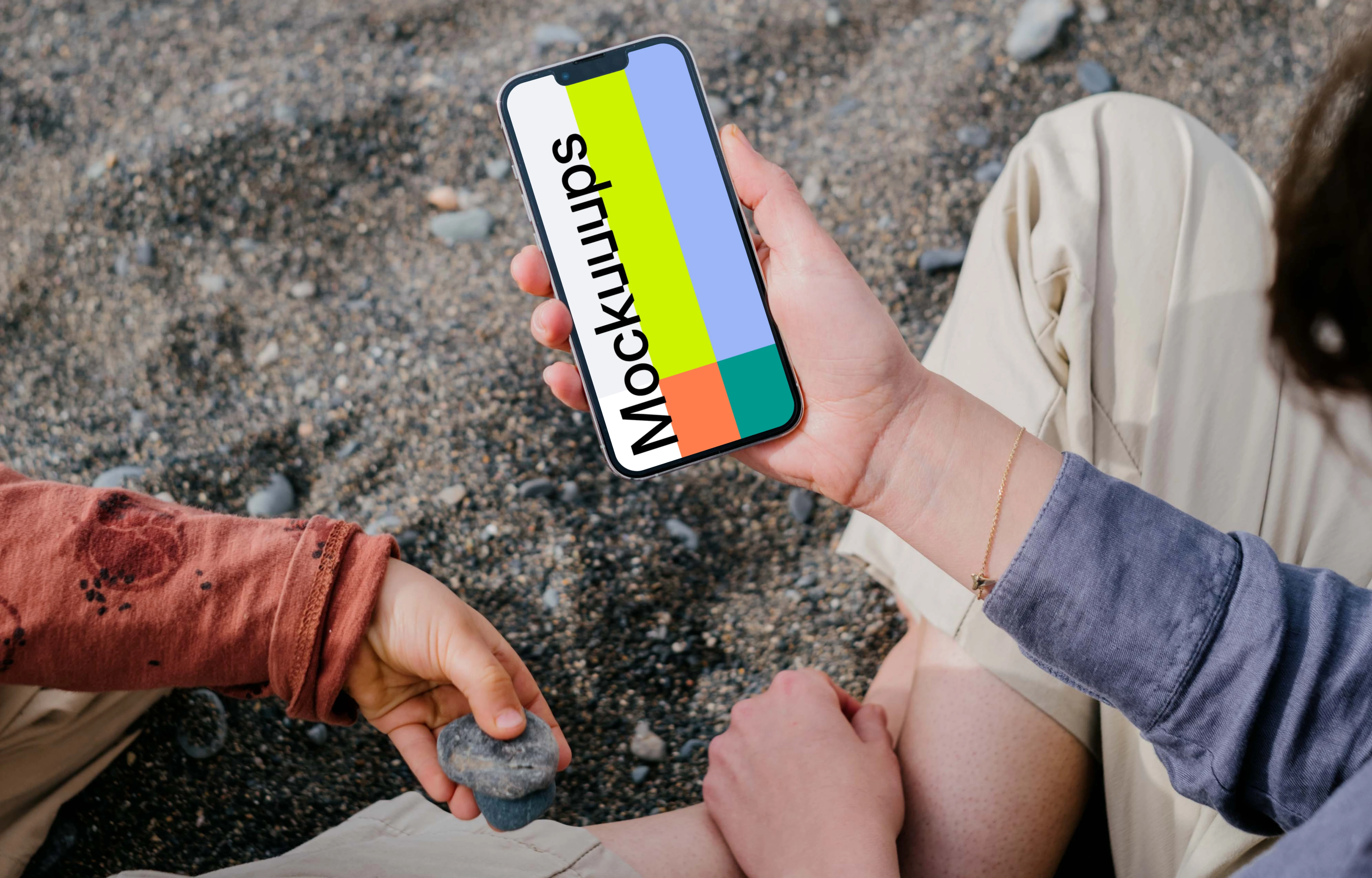 iPhone 13 Pro mockup held by a user sitting on sand