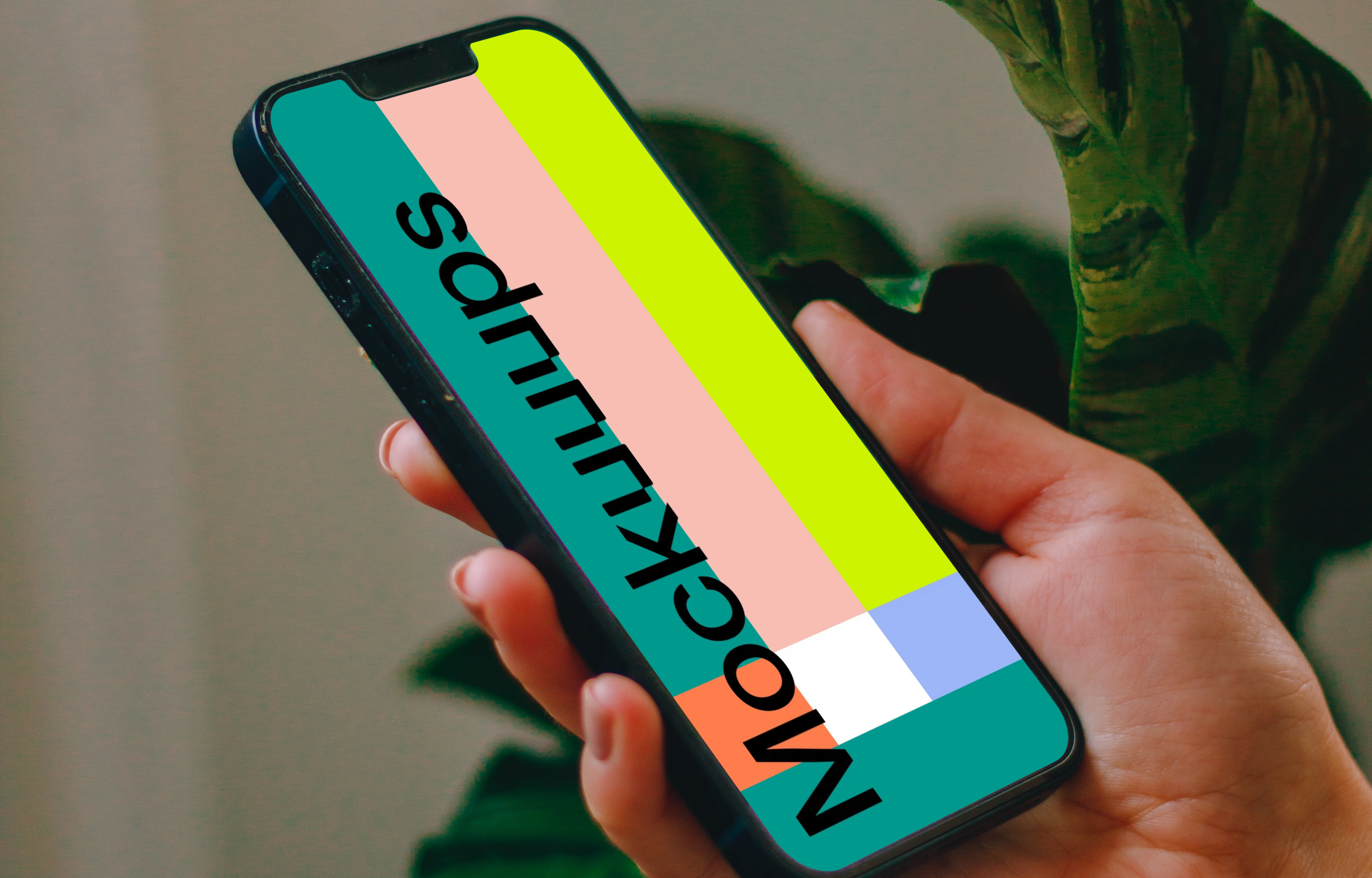 Person holding an iPhone 13 mockup with a plant in the background