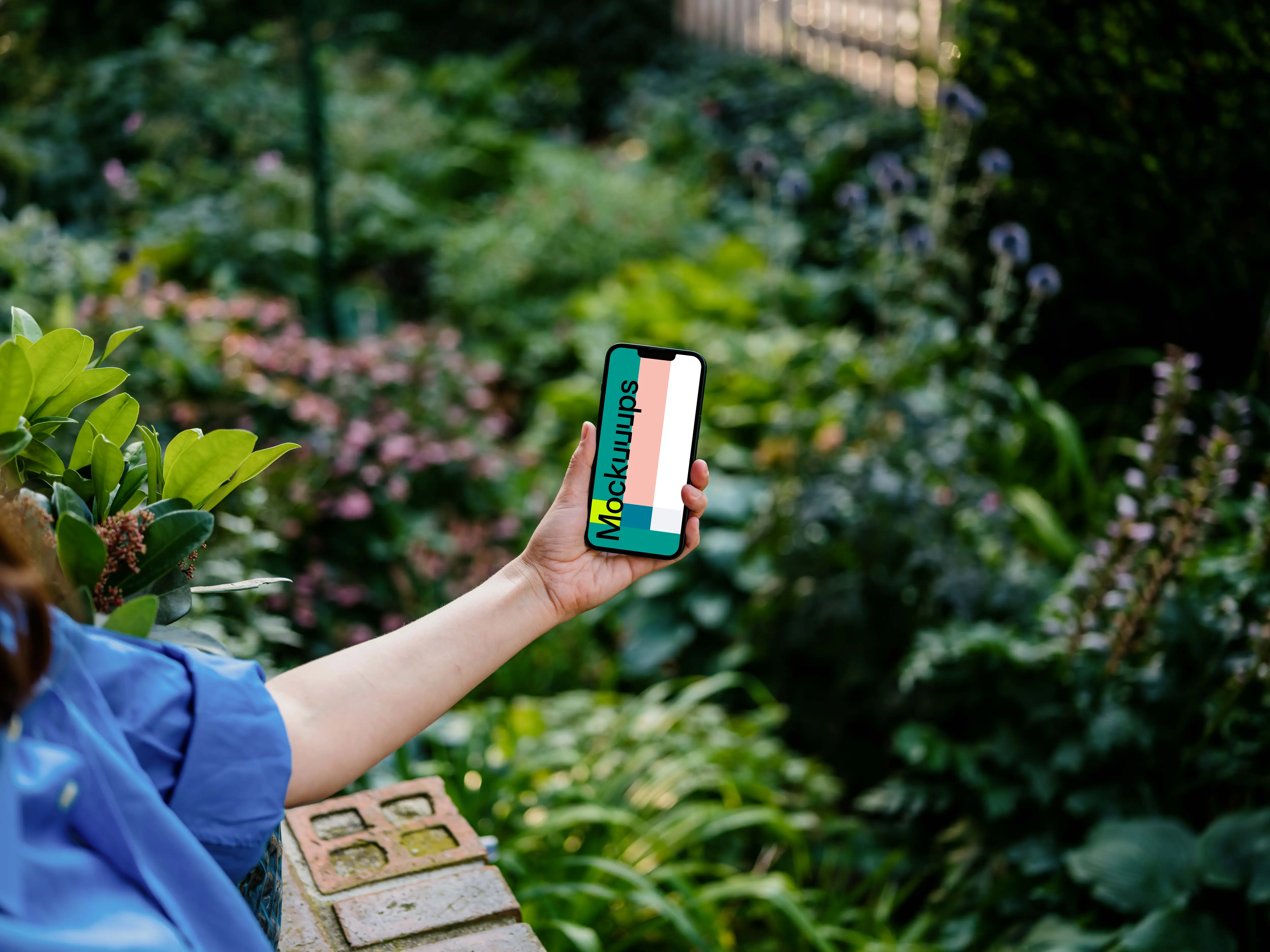 Hand holding an iPhone 13 mockup surrounded by plants